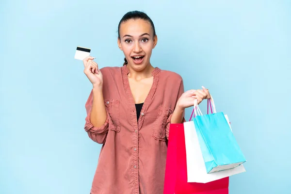 Young Arab woman isolated on blue background holding shopping bags and surprised