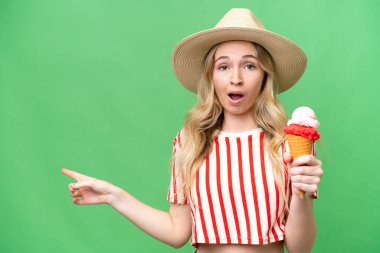 Kornet dondurması olan genç bir İngiliz kadın izole bir arka planda şaşırmış ve işaret ediyor.