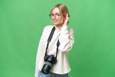 Genç fotoğrafçı İngiliz kadın, izole edilmiş arka planda bir şeyler dinlerken elini kulağına koydu.