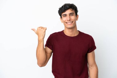 Beyaz arka planda izole edilmiş genç Arjantinli bir adam bir ürün sunmak için kenarı işaret ediyor