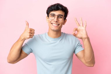 Arjantinli genç bir adam pembe arka planda gözlüklü ve tamam işareti yapıyor.