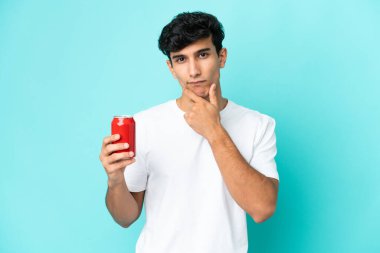 Arjantinli genç bir adam mavi arka planda izole edilmiş bir içecek tutuyor.
