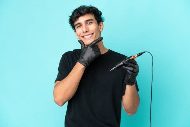 Dövme sanatçısı Arjantinli adam mavi arka planda izole edilmiş mutlu ve gülümsüyor