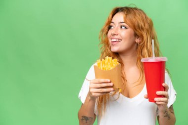 Elinde kızarmış cips ve soda tutan beyaz bir kadın yeşil ekran krom arka planda izole edilmiş.
