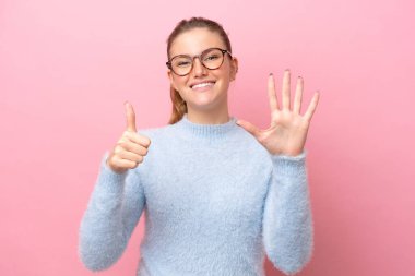 Pembe arka planda izole edilmiş genç beyaz kadın parmaklarıyla altısını sayıyor.