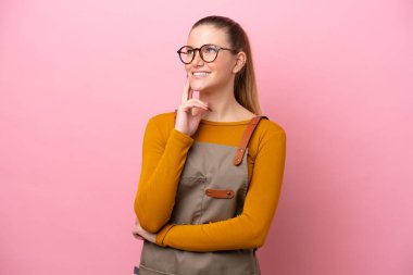 Woman with apron isolated on pink background thinking an idea while looking up