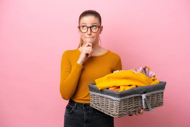 Kafkasyalı genç bir kadın pembe arka planda izole edilmiş bir sepet tutuyor. Şüpheleri var ve düşünüyor.