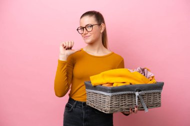 Pembe arka planda soyutlanmış, gururlu ve kendini beğenmiş bir çamaşır sepetini tutan beyaz bir kadın.