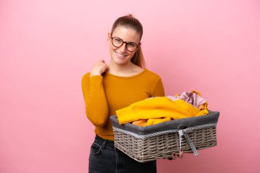 Pembe arka planda izole edilmiş çamaşır sepeti tutan beyaz bir kadın gülüyor.