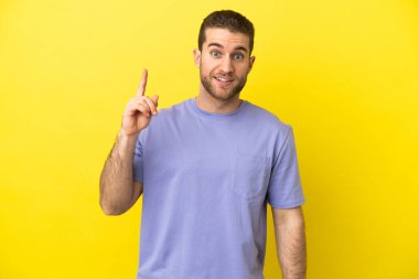 Sarışın yakışıklı adam izole edilmiş sarı arka planda bir fikir düşünüyor.