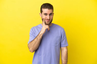 Sarışın yakışıklı adam izole edilmiş sarı arka planda ve düşünüyor