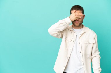 İzole edilmiş mavi arka planı olan yakışıklı sarışın adam gözlerini elleriyle kapatıyor. Bir şey görmek istemiyorum.