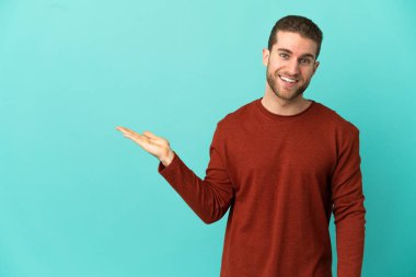 Ayrı mavi arka plan üzerinde yakışıklı sarışın bir adam. Avucunun içine reklam koymak için hayali bir alan tutuyor.