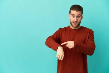 Yakışıklı sarışın, soyutlanmış mavi arka planda geç kalma jesti yapıyor.