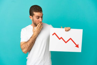İzole edilmiş mavi arkaplan üzerinde yakışıklı sarışın adam elinde azalan bir istatistik okunun işaretini tutuyor ve şaşırmış bir ifade var.