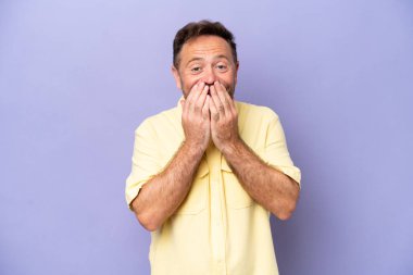 Orta yaşlı beyaz bir adam mor arka planda izole edilmiş mutlu ve gülümseyen elleriyle ağzını kapatıyor.