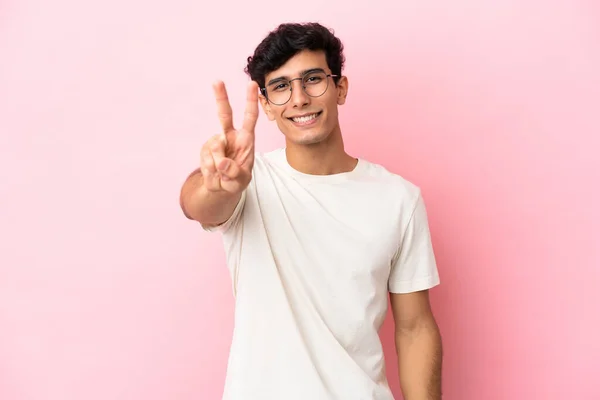 Jonge Argentijnse Man Geïsoleerd Roze Achtergrond Glimlachen Tonen Overwinning Teken — Stockfoto