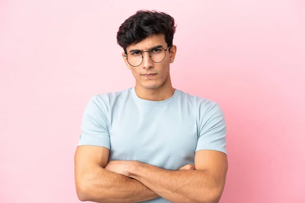 ピンクの背景に孤立した若いアルゼンチン人男性眼鏡と腕が交差 — ストック写真