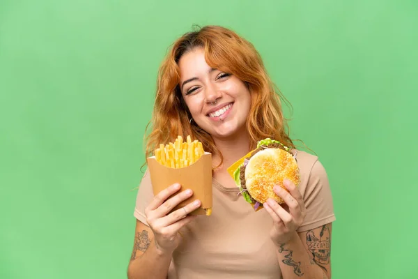 Młoda Kaukaska Kobieta Trzyma Smażone Żetony Hamburgera Izolowane Zielonym Ekranie — Zdjęcie stockowe
