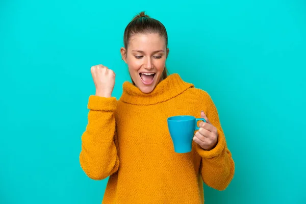 Young caucasian woman holding cup isolated on blue background celebrating a victory