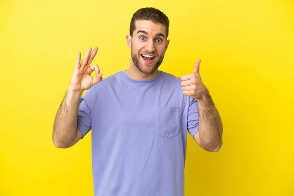 ハンサムなブロンド男上の隔離された黄色の背景ショーOk Signと親指アップジェスチャー — ストック写真