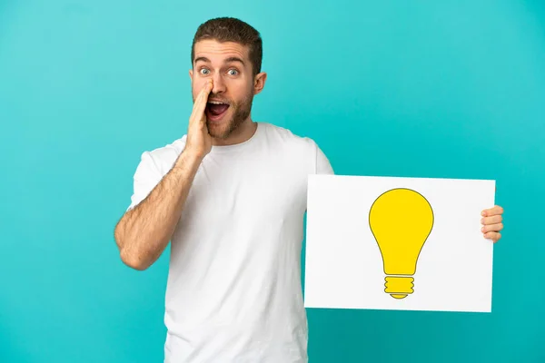 Hezké Blondýny Muž Přes Izolované Modré Pozadí Drží Plakát Žárovkou — Stock fotografie