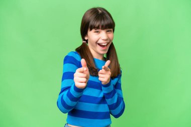 İzole edilmiş arka planda küçük beyaz kız ön tarafı işaret ediyor ve gülümsüyor.