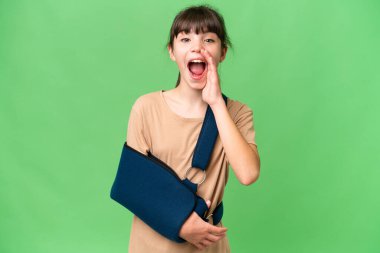 Kırık kollu küçük beyaz bir kız ve yalıtılmış arka planda askı takıyor. Şaşırmış ve şok olmuş yüz ifadesi var.