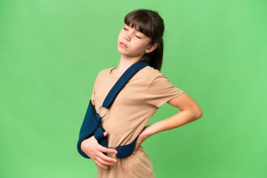 Kırık kollu küçük beyaz bir kız ve izole bir arka plan üzerinde askı takıyor. Çabaladığı için sırt ağrısı çekiyor.