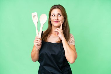 Kafkasyalı orta yaşlı bir kadın, izole bir arka plan üzerinde oklavayı tutarken kafasını kaldırıp bir fikir üretiyor.