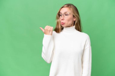 Genç sarışın kadın izole edilmiş arka planda mutsuz ve kenarı işaret ediyor.