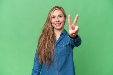 Genç sarışın kadın, izole edilmiş arka planda gülümsüyor ve zafer işareti gösteriyor.