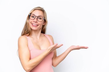 Beyaz arka planda soyutlanmış beyaz tenli genç bir kadın davet edilmek için ellerini yana uzatıyor.