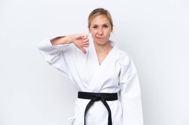 Beyaz arka planda karate yapan beyaz tenli genç bir kadın olumsuz bir ifadeyle baş parmağını aşağı gösteriyor.