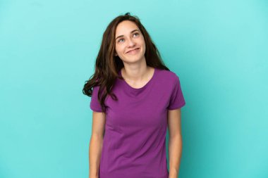 Kafkasyalı genç bir kadın mavi arka planda izole edilmiş bir şekilde yukarı bakarken bir fikir düşünüyor.