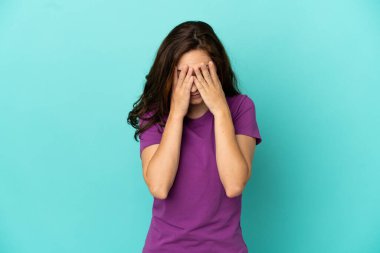 Kafkasyalı genç bir kadın mavi arka planda izole edilmiş, yorgun ve hasta bir ifadeyle.