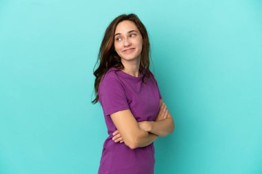 Mavi arka planda izole edilmiş, kolları bağlı ve mutlu genç beyaz bir kadın.