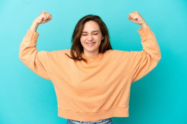 Mavi arka planda izole edilmiş beyaz bir kadın güçlü bir jest yapıyor.