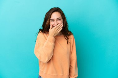 Mavi arka planda izole edilmiş genç beyaz kadın mutlu ve gülümsüyor.