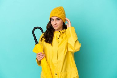 Young caucasian man holding an umbrella isolated on blue background having doubts