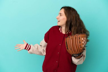 Beyzbol oynayan beyaz bir kadın mavi arka planda izole edilmiş ve sürpriz bir ifadeyle yan tarafa bakıyor.