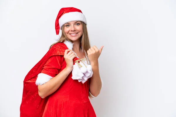 若いです白人女性として身に着けていますママノエル保持クリスマスの袋は 製品を提示するために側面を指している白い背景に隔離 — ストック写真