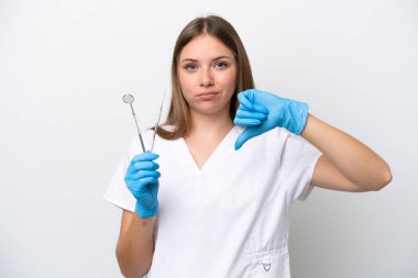 Beyaz arkaplanda izole edilmiş aletleri tutan dişçi kadın olumsuz ifade ile baş parmağını aşağı gösteriyor