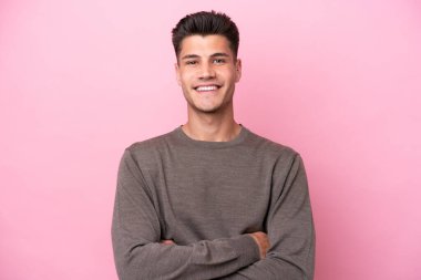 Pembe arka planda izole edilmiş genç beyaz adam kollarını ön cephede çapraz tutuyor.