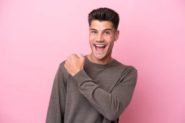 Pembe arka planda izole edilmiş genç beyaz bir adam zaferi kutluyor.