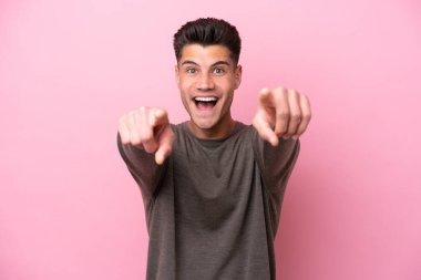 Pembe arka planda izole edilmiş genç beyaz adam şaşırmış ve ön tarafı işaret ediyor.