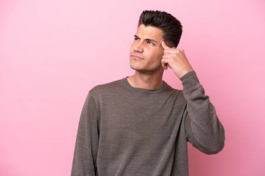 Pembe arka planda izole edilmiş genç beyaz adam deliliğin jestini yapıyor. Parmağını kafaya koyuyor.