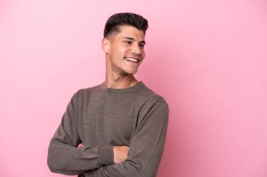 Pembe arka planda izole edilmiş, kolları bağlı ve mutlu genç beyaz bir adam.