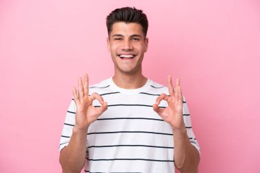 Pembe arka planda izole edilmiş beyaz bir adam iki eliyle tamam işareti gösteriyor.