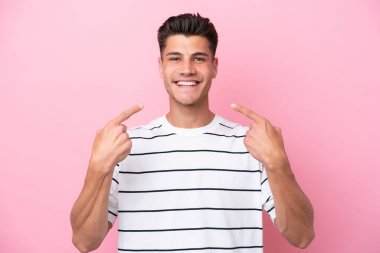 Pembe arka planda izole edilmiş genç beyaz bir adam baş parmak hareketi yapıyor.